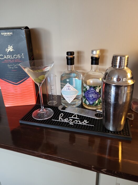 En cocktailstation med ginflaskor, drinkmätare, shaker och en martiniglas med oliver, redo för en cocktailblandning.