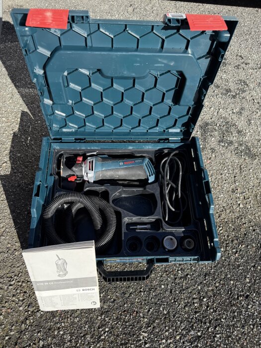 Blå Bosch GTR30 CE kakelfräs med tillbehör i plastlåda, stående på asfalt med instruktionsmanual bredvid.