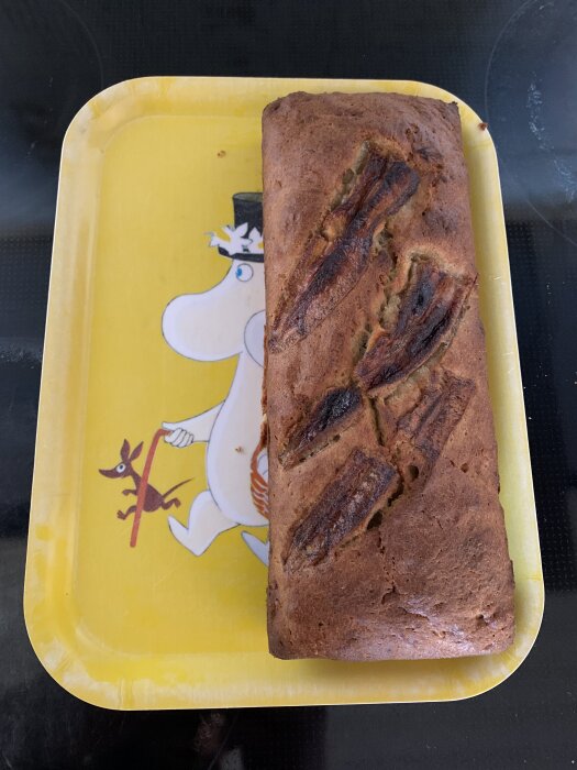 Bananbröd på en gul bricka med en vit karaktär i hatt.
