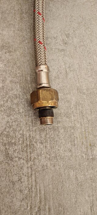 Flätad slang med koppling för vatteninstallation på betonggolv.