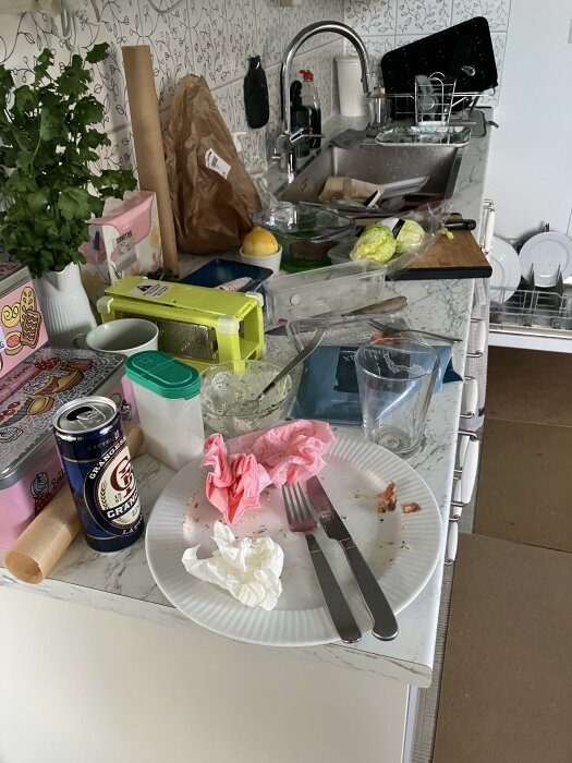 Stökig köksbänk med disk, bestick och matrester efter måltid, kaos innan städning.