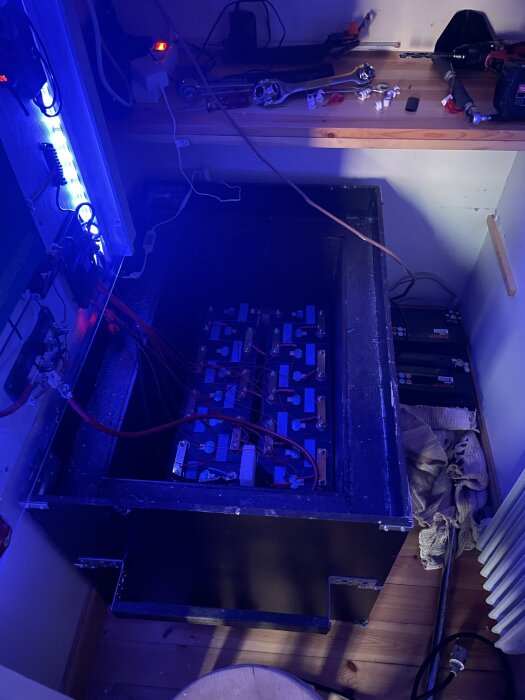 DIY 15kWh-batteri med BMS, kablar och säkringar i mörkt rum, verktyg på hyllan ovanför.