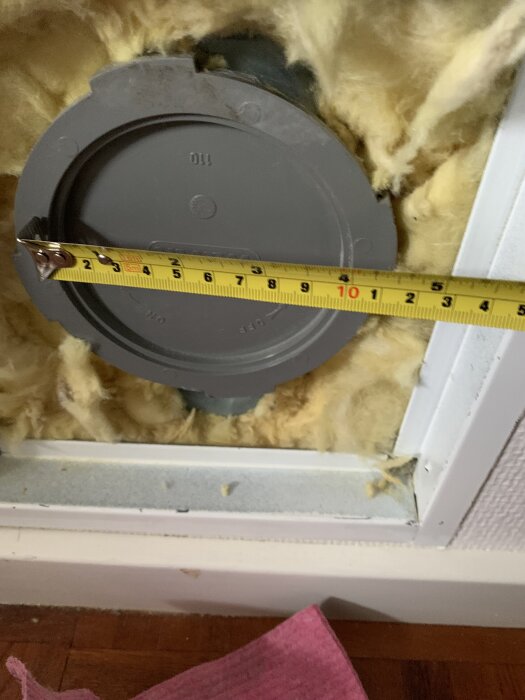 Grått täcklock med måttband för mätning, omgiven av gul isolering.