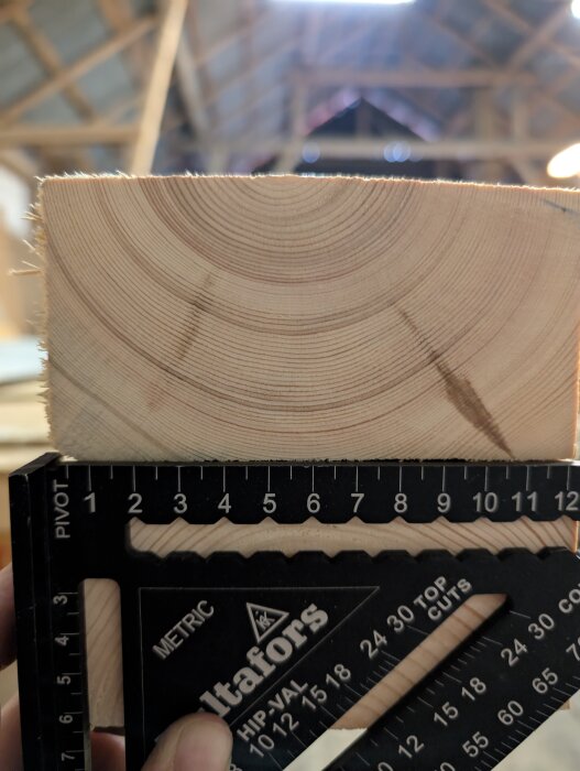 Närbild av träbit med tätt mellan årsringarna, visar en måttstock mot träet i en byggnad.