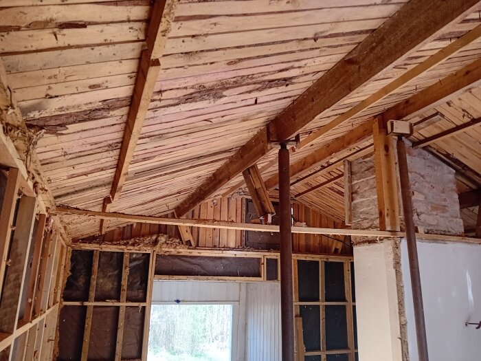 Takkonstruktion under renovering med synliga sparrar och stöttor; murstock centralt, och en träram bitvis blottad vid väggarna.