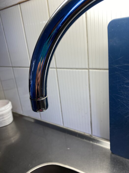 Kökskran med avtagbar sil i stål, monterad ovanför diskbänken i ett kök, med kakelvägg i bakgrunden.