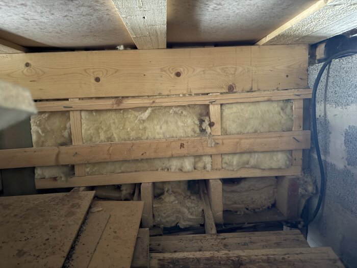 Träreglar och isolering i en grunden på ett fritidshus, med potentiell missfärgning under asfaboard.