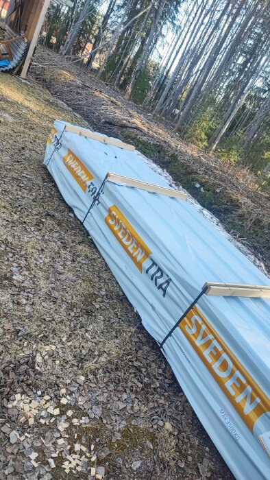 Trähög från Sveden Trä inplastad och placerad på marken, omgiven av skog.