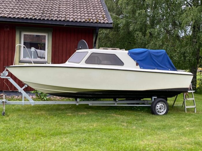 Båt på trailer, stående framför ett rött hus med blått kapell.