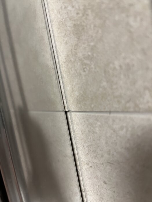 Närbild av kakelplattor i ett badrum, där fogarna är ojämna och plattornas höjd skiljer sig åt.