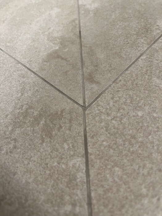 Ojämn plattsättning med synliga fogar i ett nyrenoverat badrumsgolv; plattor möts i det ojämna hörnet med varierande nivåer och färger.