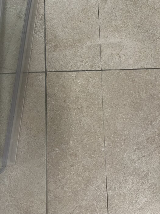 Närbild på beige kakelgolv med ojämn plattsättning där plattorna inte ligger i nivå och vissa fogar verkar flammiga i färgen.