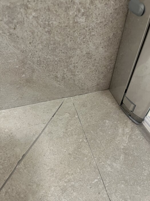 Ojämn plattsättning i ett nyrenoverat badrum med synliga skarvar, olika nivåer och flammig fog vid ett hörn.