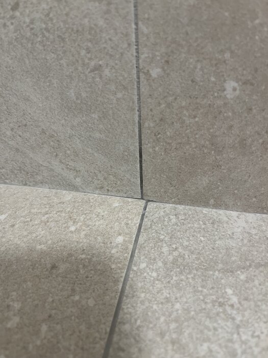 Närbild av fyra kakelplattor i ett hörn med ojämna fogar och olika nivåer i badrumsgolv.