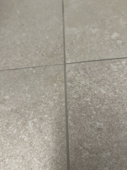 Närbild av ojämna beige kakelplattor i ett renoverat badrum, med synliga nivåskillnader och flammig fog.