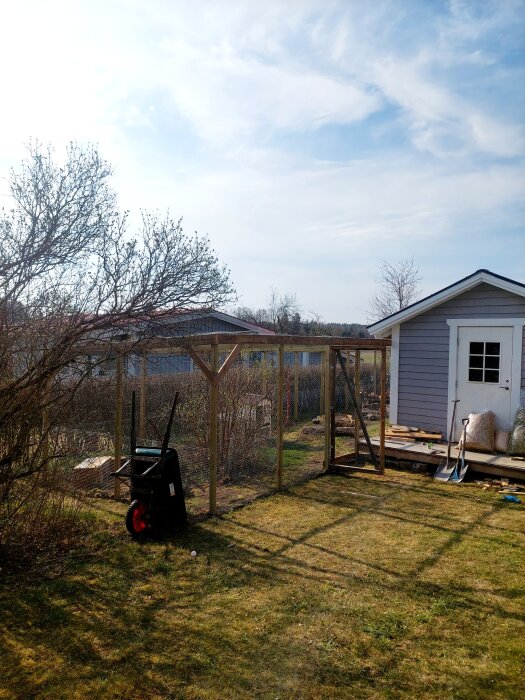 Gård med nätstängsel och litet uthus, verktyg vid sidan. Förbereds för kaniner med köpt kaninhus.
