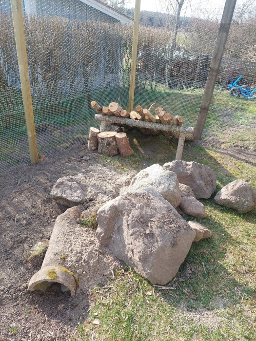 Kaninhage i trädgården med berg, jord och stockar intill staket.