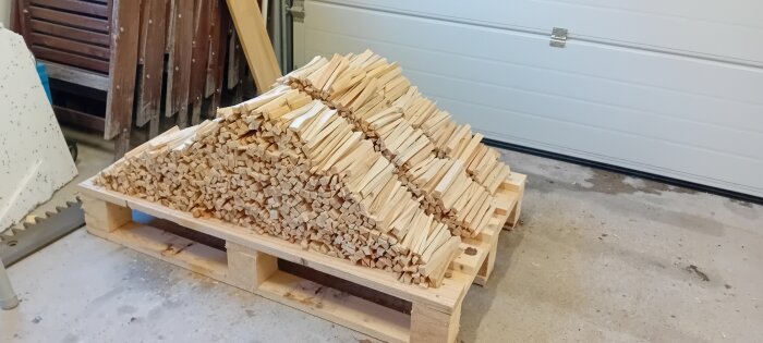 En välstaplad vedtrave på lastpall i ett garage eller förråd.