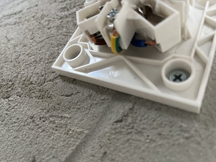 Elektrisk anslutning med kablar och skruvar monterad på en grund.