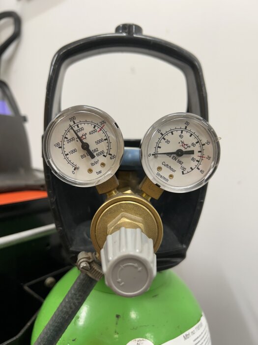 Grön gasflaska med två manometrar och en grå ventil, visar trycknivåer för svetsgas.