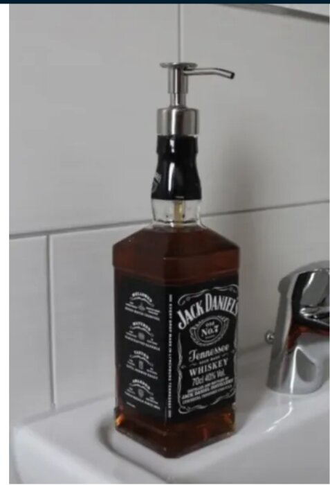 Tvålflaska gjord av en Jack Daniel's whiskeyflaska på en vit handfat med kromkran i bakgrunden.