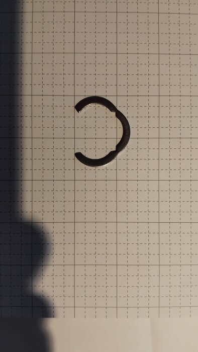 Metallring typ C-clip placerad på rutigt papper som mäter 2 cm per ruta, används för att fästa slang i solfångare.