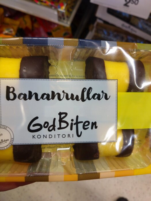 Förpackning med bananrullar från GodBiten konditori, gula med chokladändar, i butikshylla.