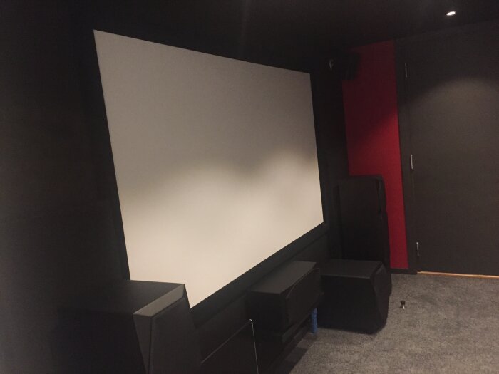 Hemmabiorum med projicerad filmduk på svart glasfiberväv, omgiven av högtalare och ljudsystem. Rummet är mörkt med diskreta färger.