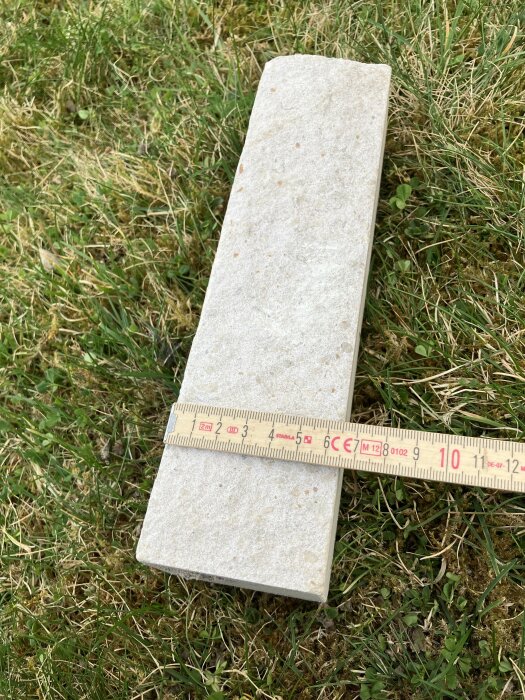 Tegelsten på gräsmatta med måttband som visar längd 250 mm.