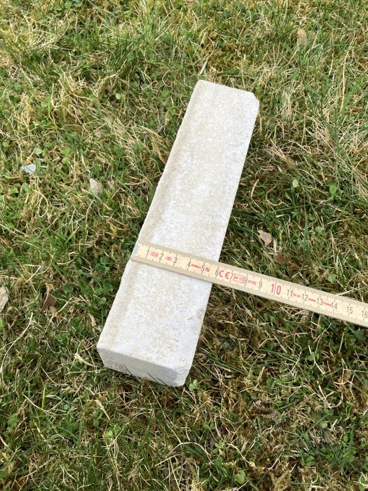 Tegelsten på gräsmatta med måttband som visar storlek, kan användas för byggen.