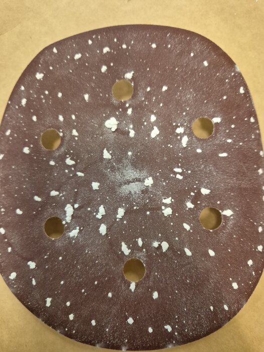 Slitet sandpapper för excenterslip, med vita rester på ytan efter slipning av målad furu.