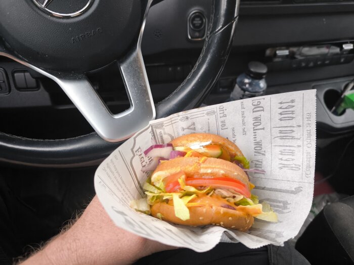 En dubbel cheeseburgare hålls i en bil, placerad framför en ratt.