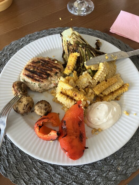 Grillad kycklingburgare, majs, paprika, romansallad, svamp och yoghurt med mangochutney på en tallrik.