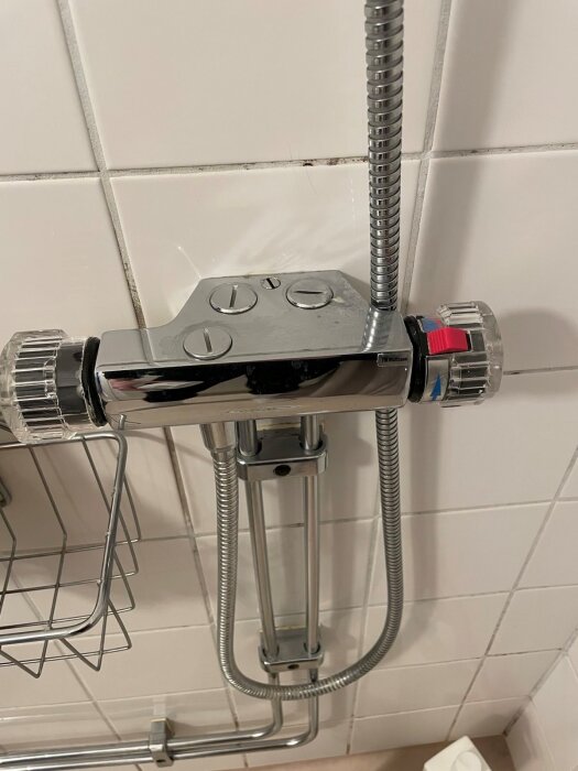 Duschblandare med två reglage mot kaklad vägg, kopplad med metallslangar.