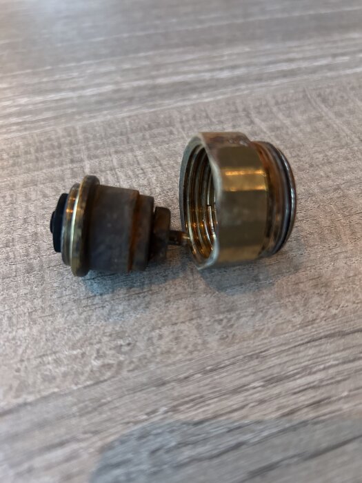 Ventil med mässingsmutter från en golvvärmefördelare, synlig packning och gängor, placerad på ett trägolv.