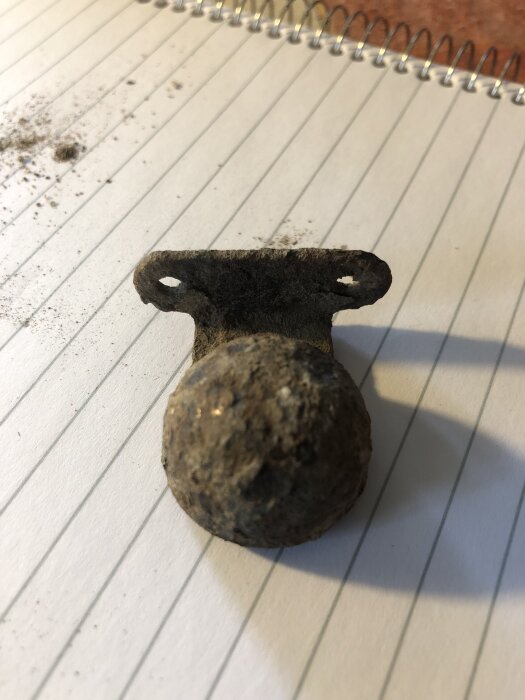 Svagt magnetisk metallföremål på linjerat anteckningsblock, cirka 4x2,5 cm.