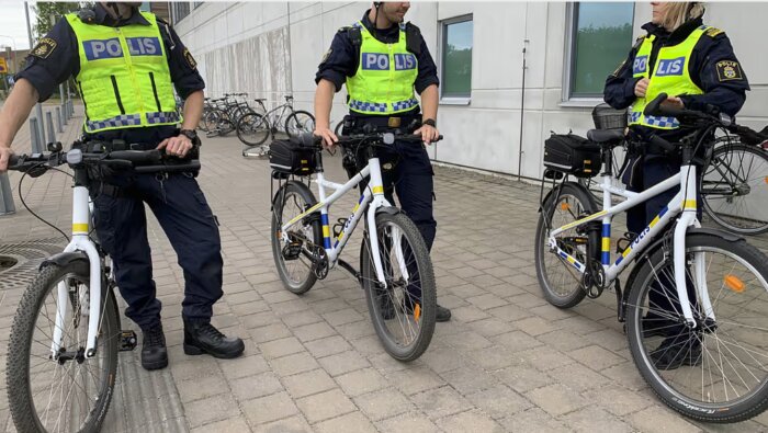 Poliser i uniform står med sina cyklar utanför en byggnad, redo för patrull.