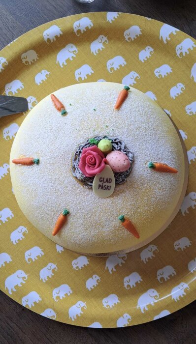 Påskig tårta med marsipanmorötter och påskdekorationer, liggande på en gul tallrik med elefantmönster.
