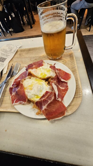 En tallrik med spansk skinka och stekta ägg, serverad med en stor öl på ett café i Madrid.