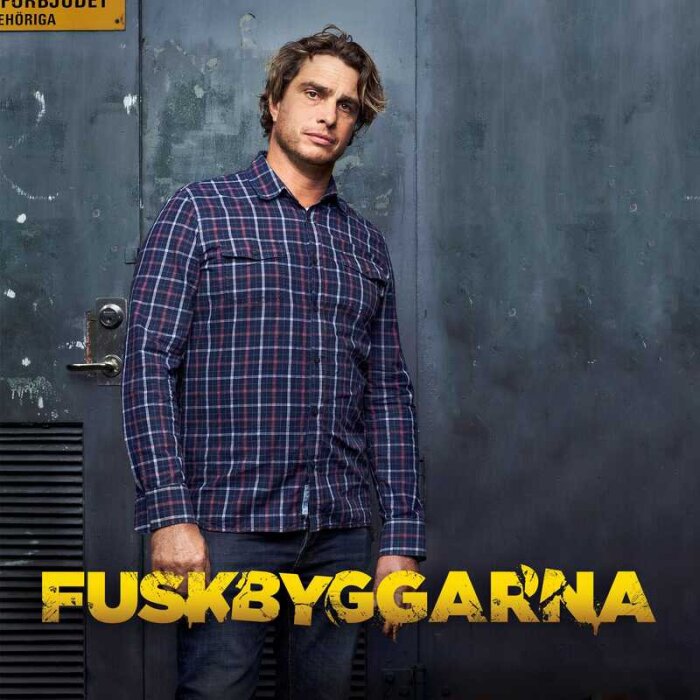 Man i rutig skjorta framför en metallvägg med texten "FUSKBYGGARNA" i gult.