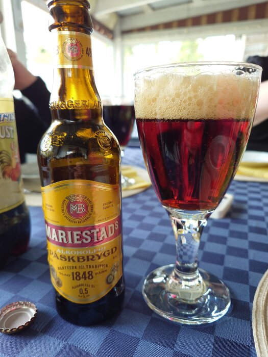 Flaska Mariestads påskbrygd och glas med mörk dryck på dukat bord, feststämning.