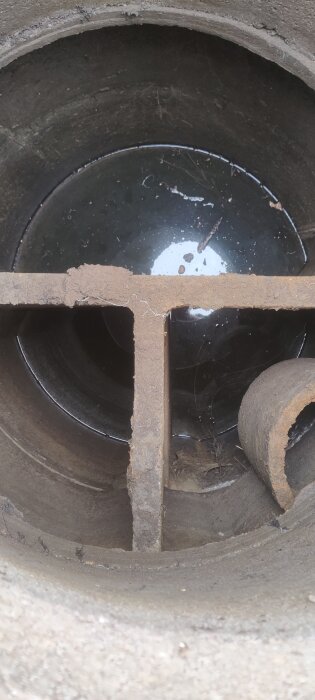 Närbild av en gammal trekammarbrunn i betong med vatten i botten och en skiljevägg synlig.