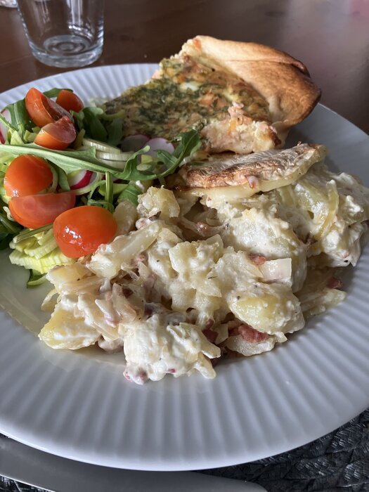 Tallrik med tartiflette, paj med rökt lax och en sallad med gröna blad och tomater.