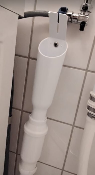 Anslutning av ett vitt avloppsrör i ett badrum, monterat mot väggen.