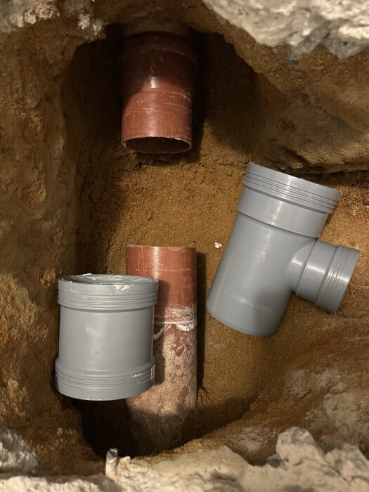 Rörsystem under mark med grå grenrör och rött rör i jord. En del av röret kan tas av för att underlätta montering.