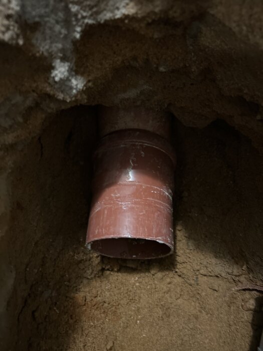 Rött rör av PVC delvis installerat i en jordhålighet, del av ett VVS-projekt.