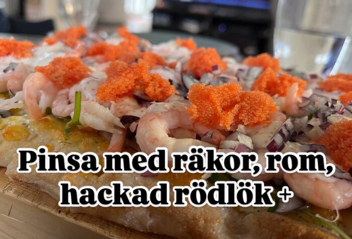 Pinsa toppad med räkor, röd rom, hackad rödlök, gräddfil och svartpeppar på en träskärbräda.