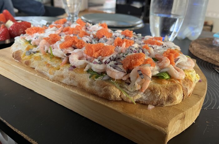 Pinsa toppad med räkor, rödlök, dill, citron, gräddfil och rom, serverad på en trätallrik.