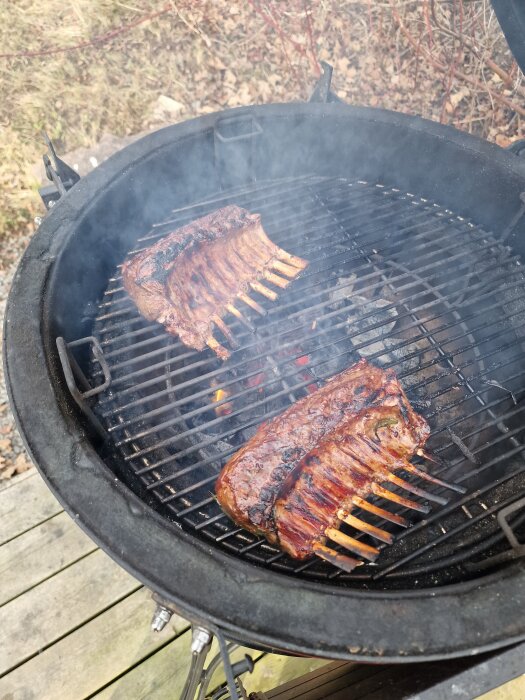 Lammracks grillas på en kolgrill utomhus, omgivna av rök och glödande kol.