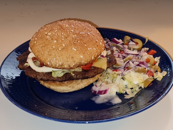 Hamburgare med västerbottenost och en blandad sallad med vitlöksdressing på en blå tallrik.